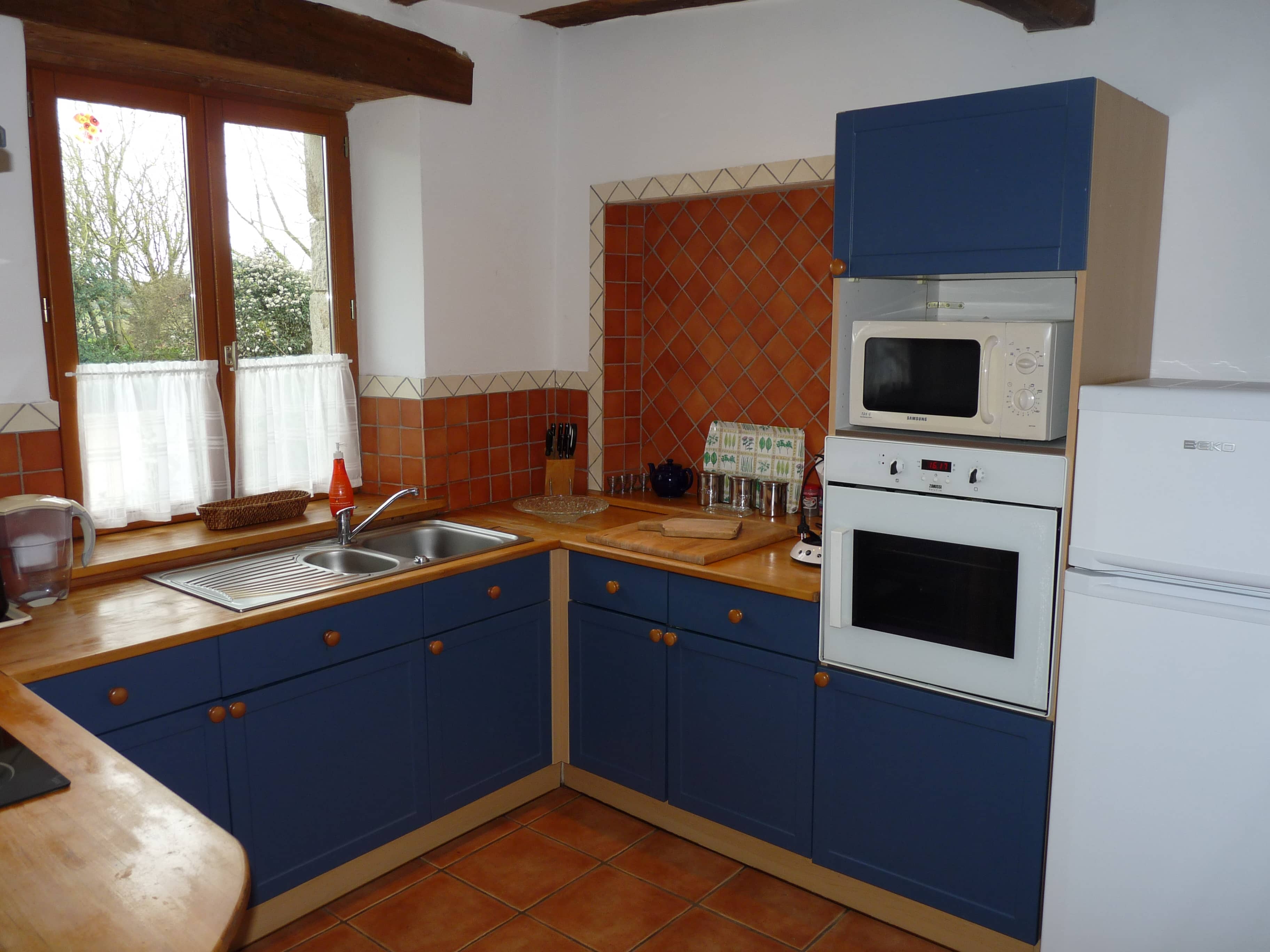 Kitchen of La Julerie cottage in Brittany, France, with a dining table, high-end appliances, and a view of the garden. Ideal for preparing holiday meals with family or friends.